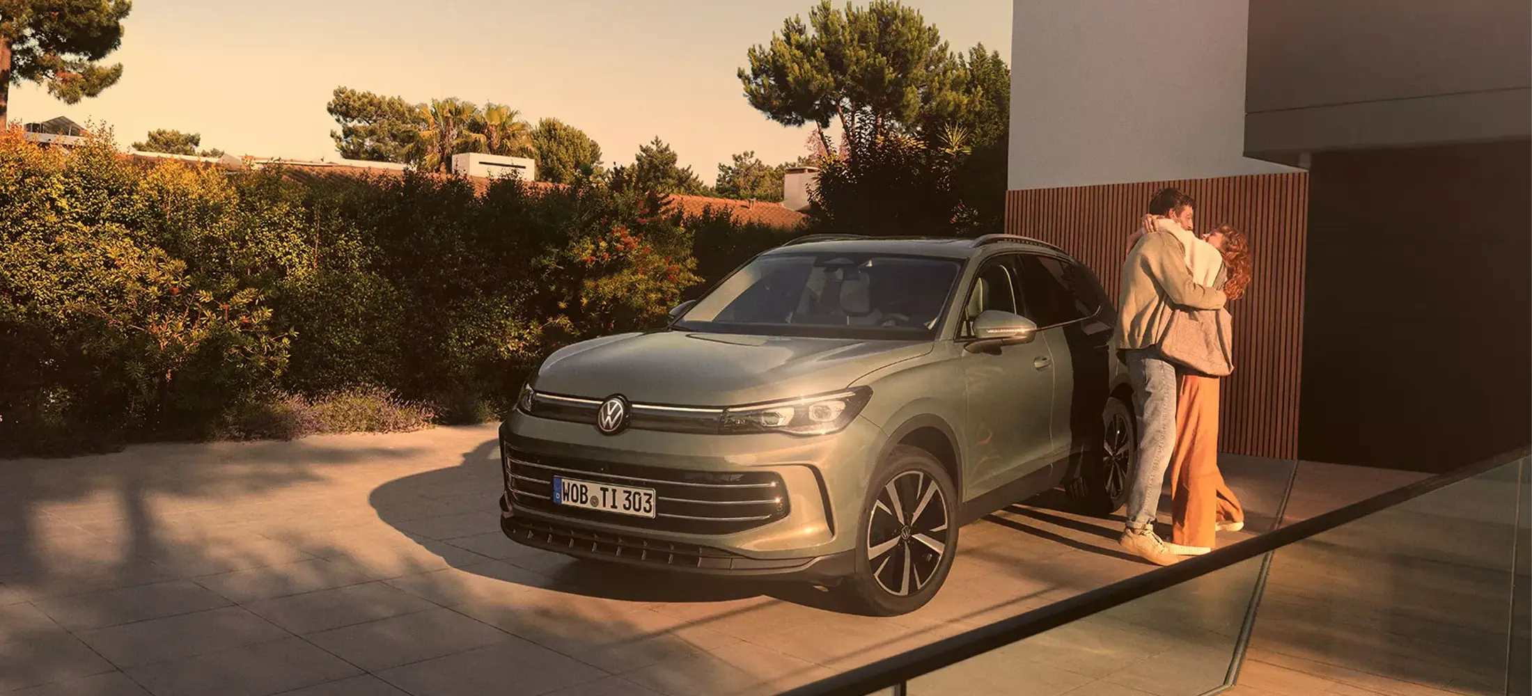 Tiguan vor einem Haus, daneben Pärchen, das sich umarmt